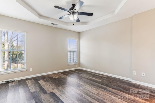 empty room with dark wood-type flooring, ceiling fan, and a tray ceiling