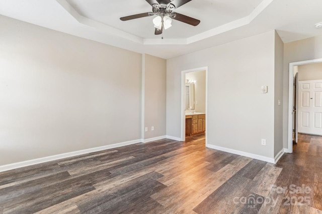 empty room with a raised ceiling, ceiling fan, and dark hardwood / wood-style flooring