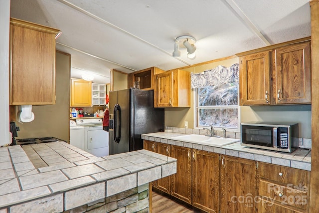 kitchen with black fridge, tile counters, washer and clothes dryer, and sink