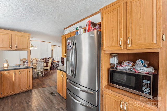 kitchen with a textured ceiling, stainless steel appliances, ornamental molding, dark countertops, and dark wood finished floors