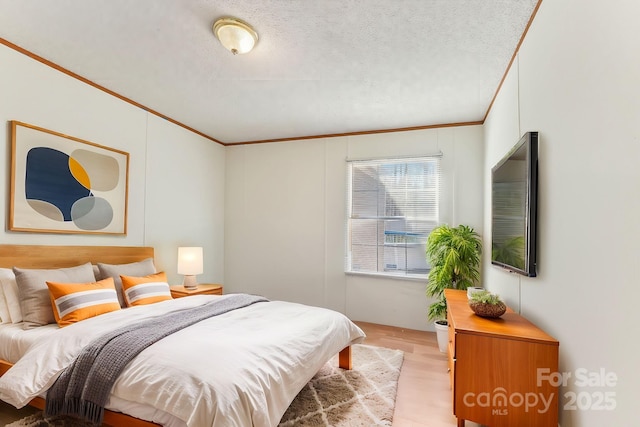 bedroom with a textured ceiling, ornamental molding, and light wood-style floors