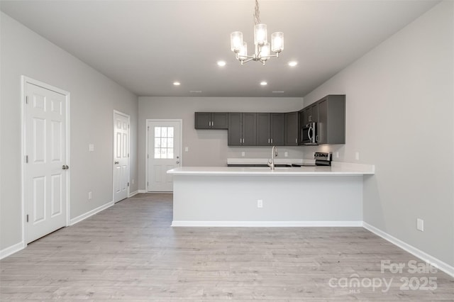 kitchen with gray cabinetry, light wood-type flooring, appliances with stainless steel finishes, kitchen peninsula, and pendant lighting