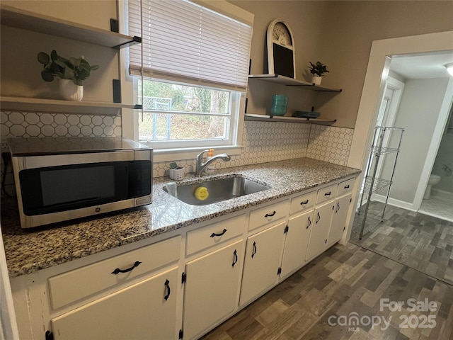 kitchen featuring dark wood-type flooring, sink, light stone countertops, decorative backsplash, and white cabinets