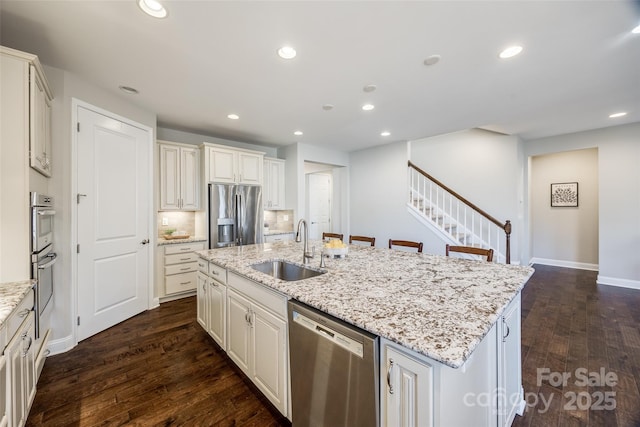 kitchen featuring sink, stainless steel appliances, dark hardwood / wood-style floors, light stone countertops, and a center island with sink