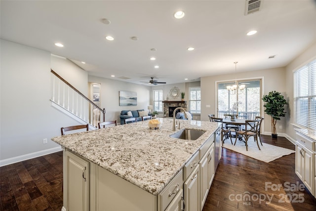 kitchen with sink, a stone fireplace, light stone countertops, a center island with sink, and decorative light fixtures