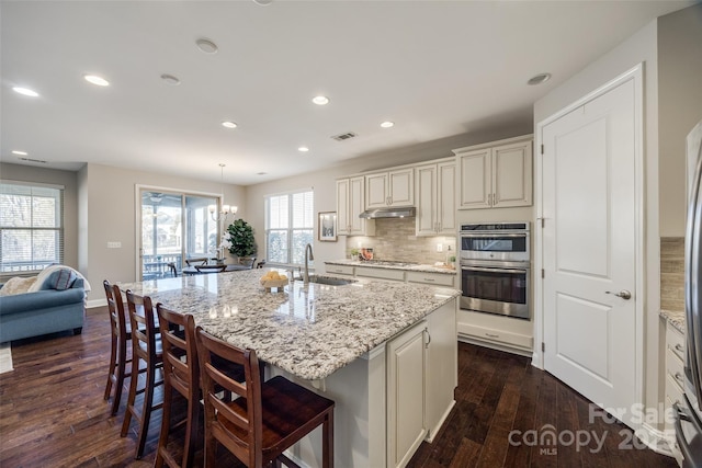 kitchen featuring stainless steel appliances, sink, a center island with sink, and light stone counters