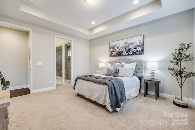 carpeted bedroom with ensuite bathroom and a tray ceiling