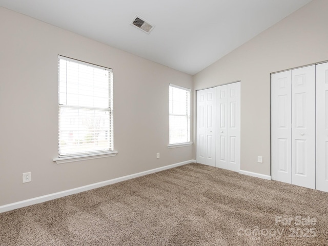 unfurnished bedroom featuring multiple windows, vaulted ceiling, multiple closets, and carpet flooring