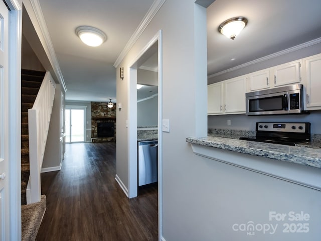 kitchen with ornamental molding, stainless steel appliances, a stone fireplace, and white cabinets