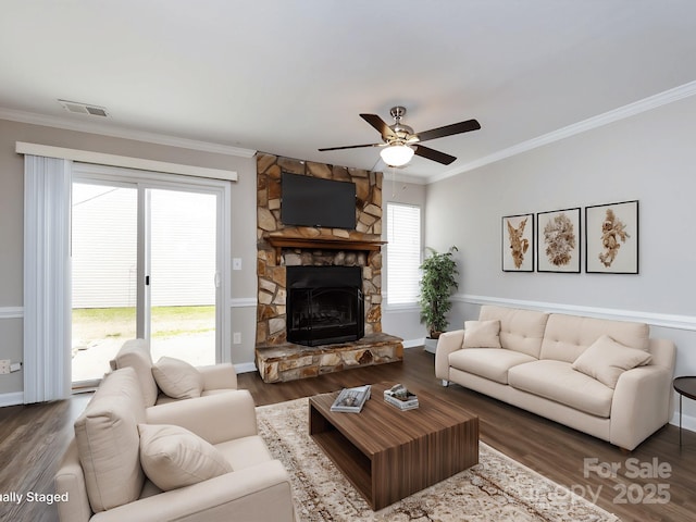 living room with ornamental molding, plenty of natural light, dark wood-type flooring, and a stone fireplace