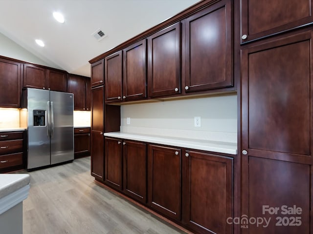 kitchen featuring vaulted ceiling, dark brown cabinets, light hardwood / wood-style floors, and stainless steel fridge with ice dispenser