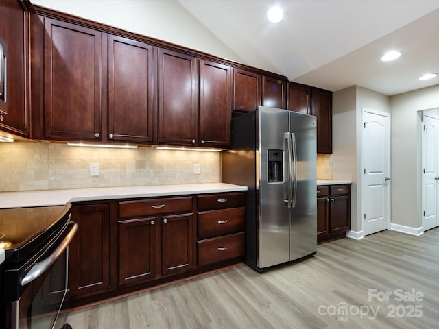 kitchen featuring vaulted ceiling, appliances with stainless steel finishes, light hardwood / wood-style floors, and decorative backsplash