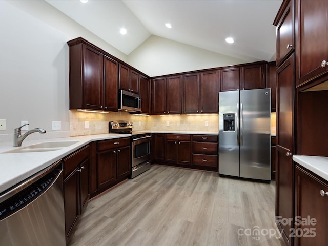 kitchen with lofted ceiling, sink, decorative backsplash, light hardwood / wood-style floors, and stainless steel appliances