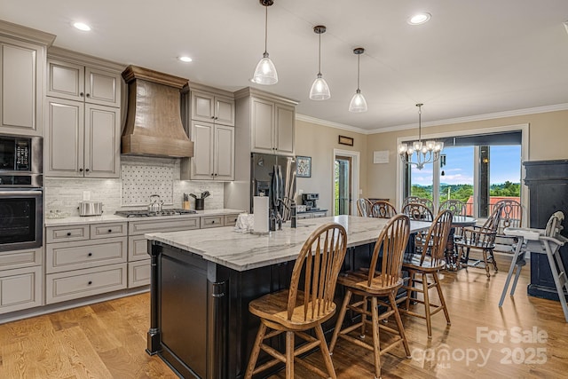 kitchen featuring stainless steel appliances, custom exhaust hood, hanging light fixtures, and a center island with sink