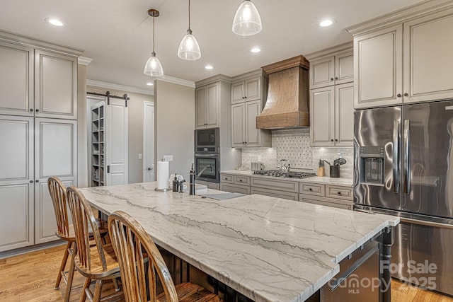 kitchen with stainless steel appliances, an island with sink, a barn door, and custom range hood