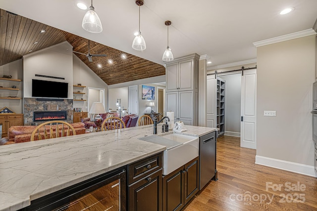 kitchen featuring hanging light fixtures, wine cooler, stainless steel dishwasher, a barn door, and light wood-type flooring