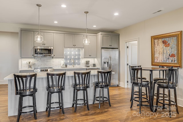 kitchen featuring a breakfast bar, gray cabinetry, a center island, appliances with stainless steel finishes, and pendant lighting