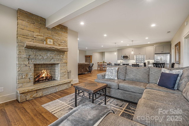 living room with beam ceiling, a stone fireplace, and dark wood-type flooring