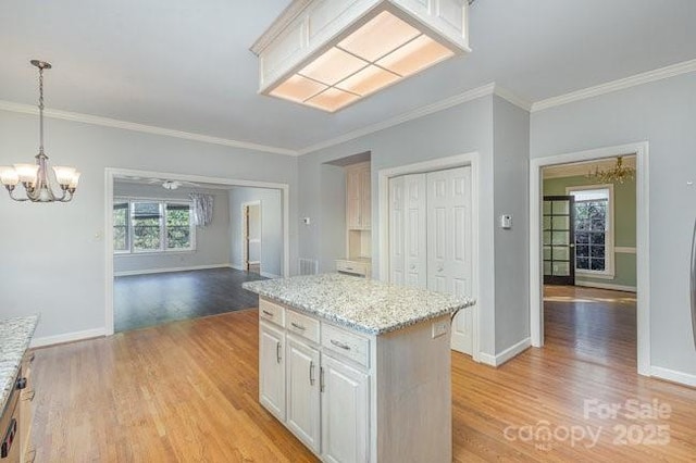 kitchen featuring hanging light fixtures, a center island, light stone counters, white cabinets, and light wood-type flooring