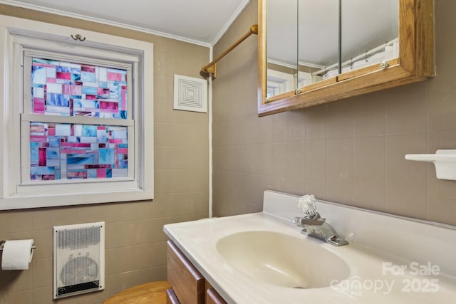 bathroom with heating unit, vanity, crown molding, and tile walls