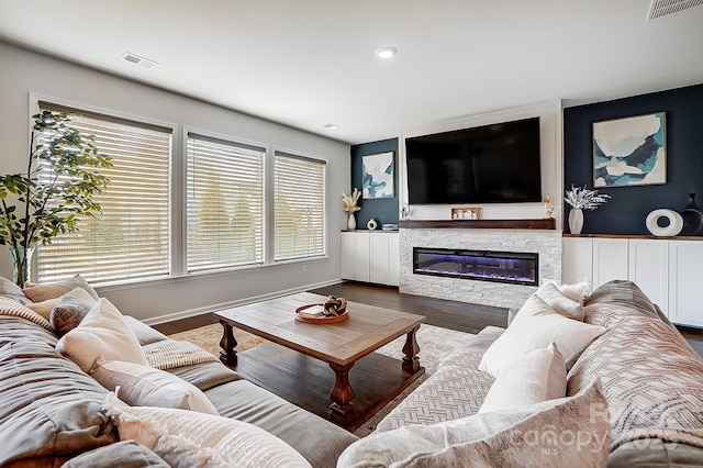 living room with a glass covered fireplace, visible vents, baseboards, and wood finished floors