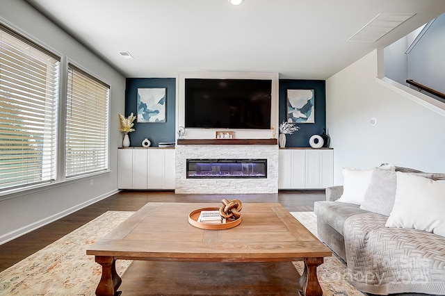 living room featuring dark wood-style floors, visible vents, a fireplace, and baseboards