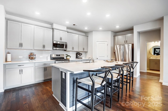 kitchen featuring a kitchen island with sink, a kitchen breakfast bar, light countertops, appliances with stainless steel finishes, and gray cabinets