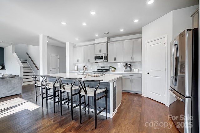 kitchen featuring a breakfast bar area, open floor plan, a kitchen island with sink, stainless steel appliances, and light countertops