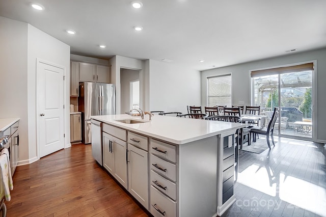 kitchen with a kitchen island with sink, light countertops, a sink, and gray cabinetry