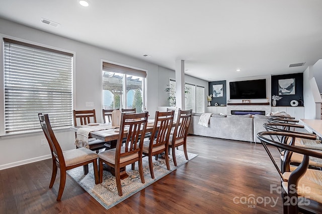 dining space featuring dark wood-style flooring, a fireplace, visible vents, and baseboards