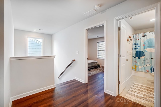 hall featuring dark wood-style floors, baseboards, visible vents, and an upstairs landing