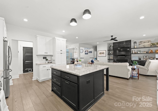 kitchen featuring ceiling fan with notable chandelier, stainless steel refrigerator, white cabinetry, a center island, and light wood-type flooring