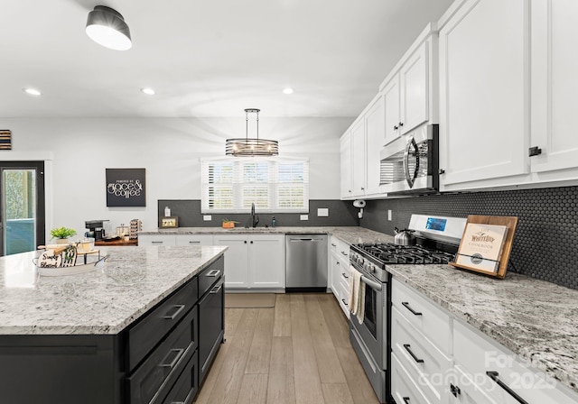 kitchen with sink, hanging light fixtures, plenty of natural light, appliances with stainless steel finishes, and white cabinets