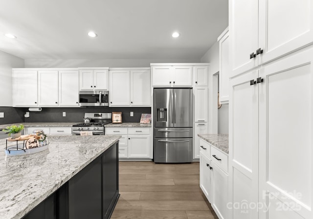 kitchen with appliances with stainless steel finishes, dark hardwood / wood-style floors, light stone countertops, and white cabinets