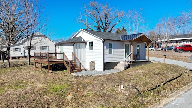 view of front of property with a deck, a shingled roof, and a front yard