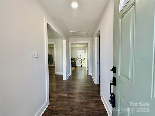 hallway with dark wood finished floors, attic access, and baseboards