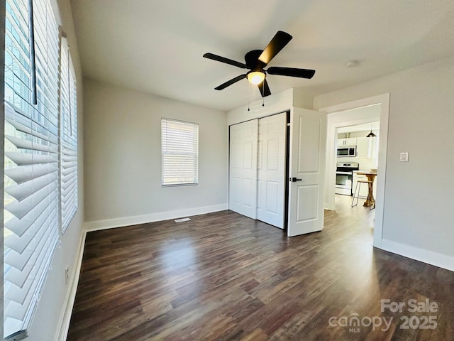 unfurnished bedroom featuring a closet, dark wood finished floors, baseboards, and ceiling fan