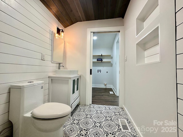 half bath with wooden walls, visible vents, toilet, wood ceiling, and a sink