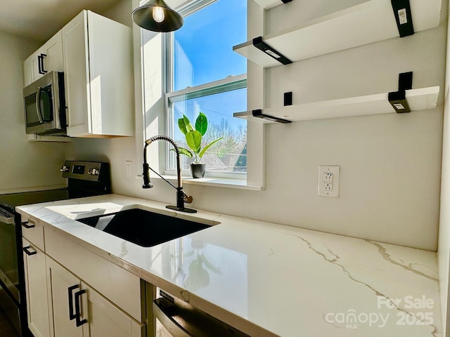 kitchen with a sink, white cabinets, appliances with stainless steel finishes, light stone countertops, and open shelves