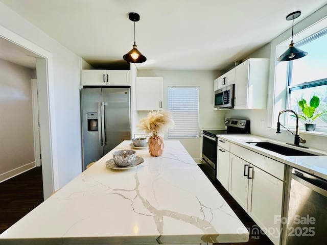 kitchen with white cabinets, light stone counters, appliances with stainless steel finishes, hanging light fixtures, and a sink