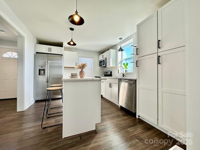 kitchen with a kitchen island, white cabinets, hanging light fixtures, appliances with stainless steel finishes, and light countertops