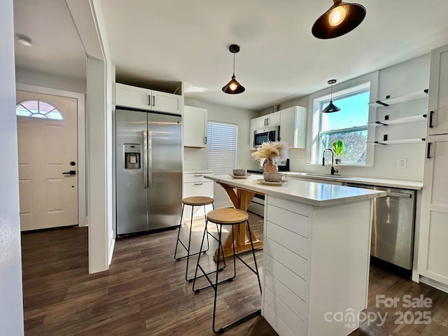 kitchen with white cabinets, appliances with stainless steel finishes, hanging light fixtures, light countertops, and a sink