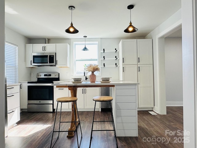 kitchen with white cabinets, a breakfast bar, dark wood-style flooring, stainless steel appliances, and light countertops