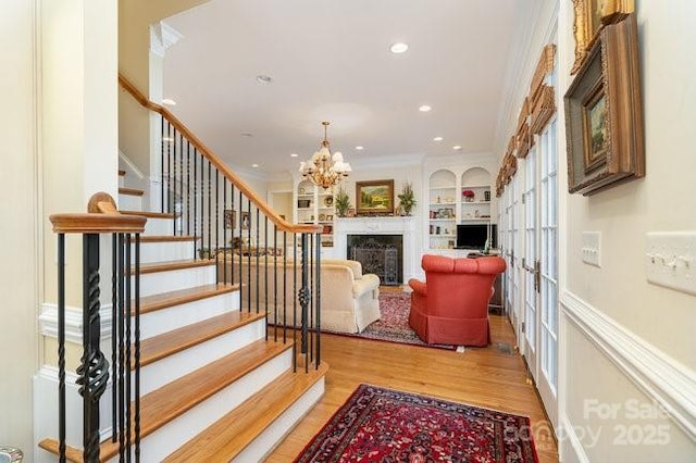 stairs featuring built in shelves, ornamental molding, an inviting chandelier, and hardwood / wood-style floors