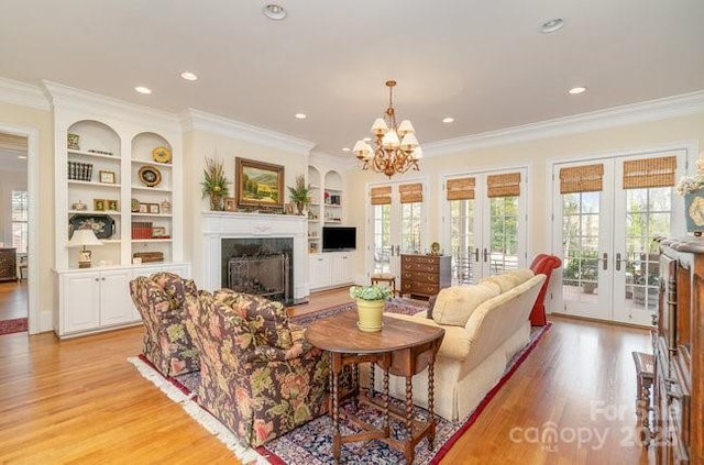 living room featuring a fireplace, ornamental molding, light hardwood / wood-style floors, built in shelves, and french doors