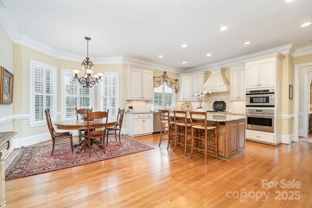 kitchen featuring appliances with stainless steel finishes, custom range hood, a kitchen island, decorative light fixtures, and light wood-type flooring