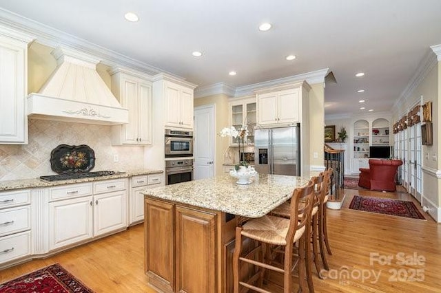 kitchen featuring crown molding, premium range hood, appliances with stainless steel finishes, a center island, and white cabinets