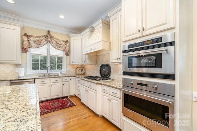 kitchen with premium range hood, sink, tasteful backsplash, appliances with stainless steel finishes, and light stone countertops