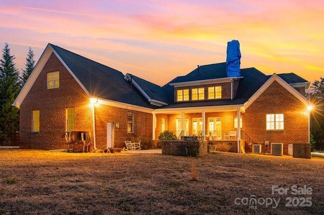 back house at dusk featuring cooling unit and covered porch