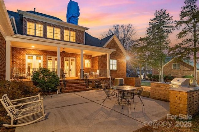 back house at dusk with central AC unit, a patio area, and exterior kitchen